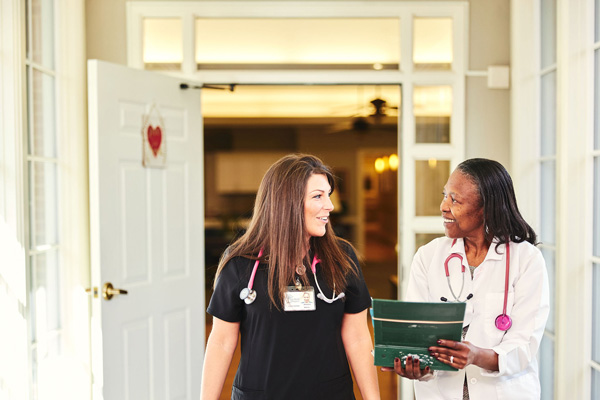 A Hospice nurse and physician walk down a hallway the the Dozier Hospice House discussing patient services and an individualized care plan for a patient.