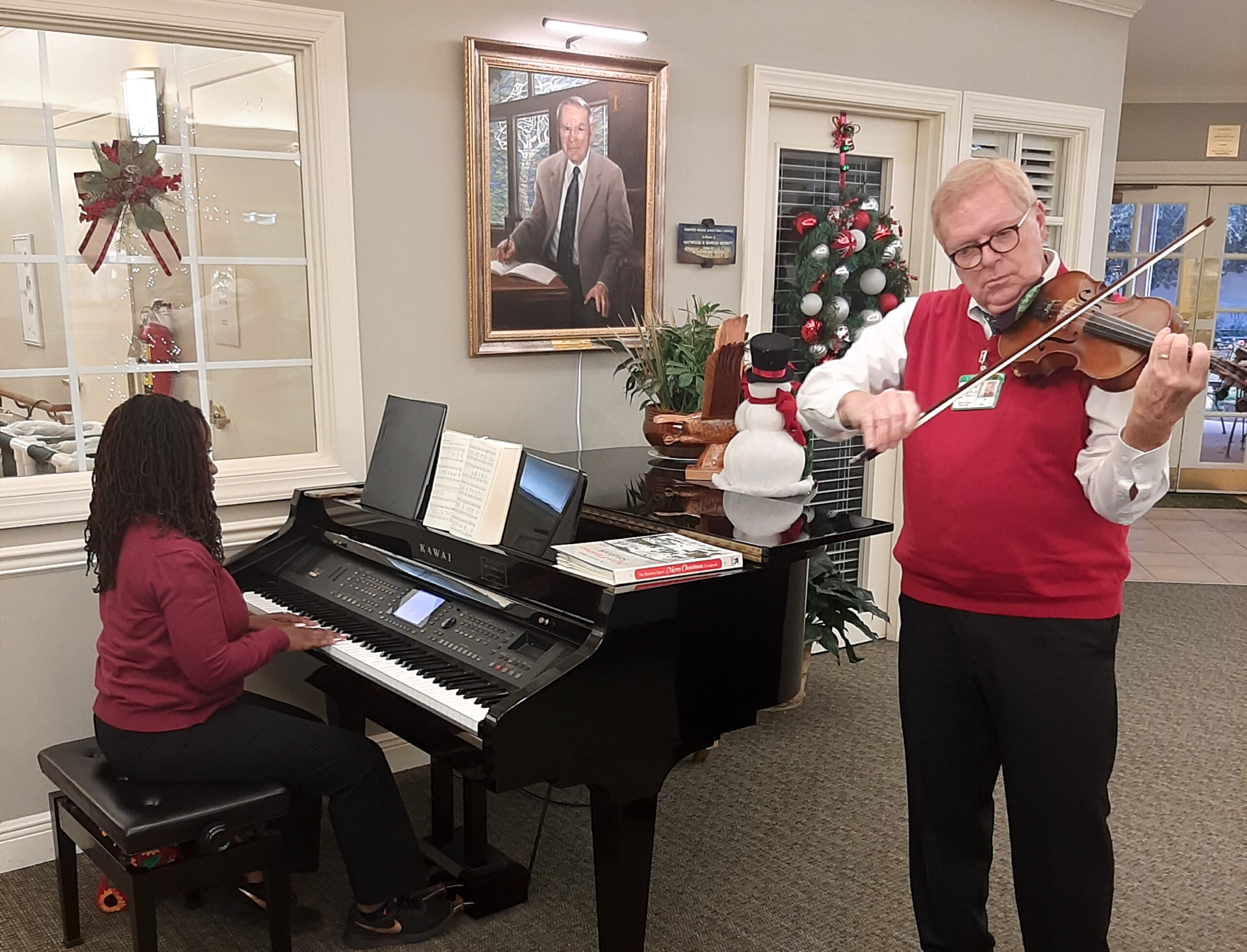 A woman sits playing the piano while a man stands next to her playing the violin at the Dozier Hospice House